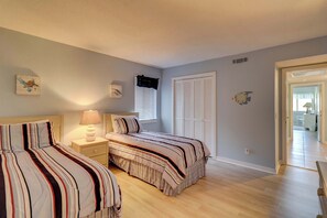 A bedroom with two beds, a nightstand with a lamp, a window with blinds, and a door leading to another room. - Sea Pines condo with amazing golf course view, pool, & balcony - walk to beach (Hilton Head)