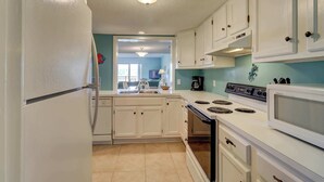 Una cocina con gabinetes blancos, estufa, microondas y refrigerador.