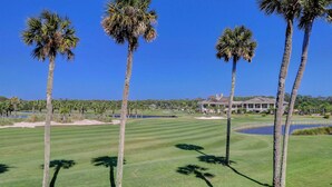 Un campo de golf con palmeras, una casa grande al fondo y un cielo azul despejado.
