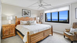Una camera da letto con un grande letto, una ventola a soffitto, una finestra con vista e una sedia in vimini.
