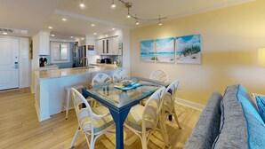Uma cozinha moderna com armários brancos, uma ilha central e um espaço de jantar com mesa de vidro e cadeiras brancas.