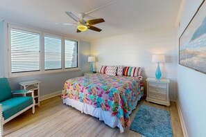 Un dormitorio con cama, ventilador de techo, mesita de noche, lámpara, silla y ventana con persianas.