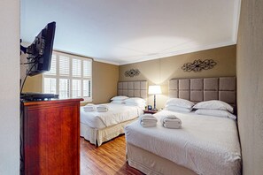Ein Hotelzimmer mit zwei Betten, einem Schreibtisch, einem Fernseher, einer Lampe und einer Wanddekoration.