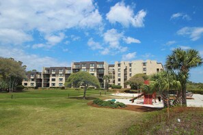 A residential building with multiple balconies, a playground, and a well-maintained lawn. - A Relaxing Getaway with Shared Pools and Hot Tub in an Oceanfront Villa (Hilton Head)