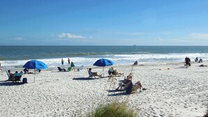Una platja amb gent relaxant sota ombrel·les, algunes assegudes en cadiretes i altres passejant al llarg de la riba.