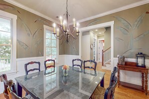 A dining room with a glass table, chairs, a chandelier, and wall murals.