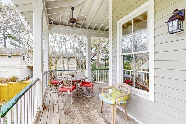 A covered porch with a table and chairs, a wooden railing, and a window with a view of the neighborhood.