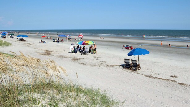 Ein Strand mit Sonnenschirmen, Liegestühlen und Personen.