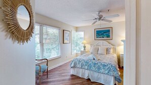 Ein Schlafzimmer mit Bett, Deckenventilator, Wandspiegel und einem Fenster mit Jalousien.