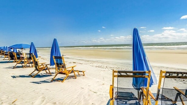 Een strand met rijen ligbedden en blauwe parasols.