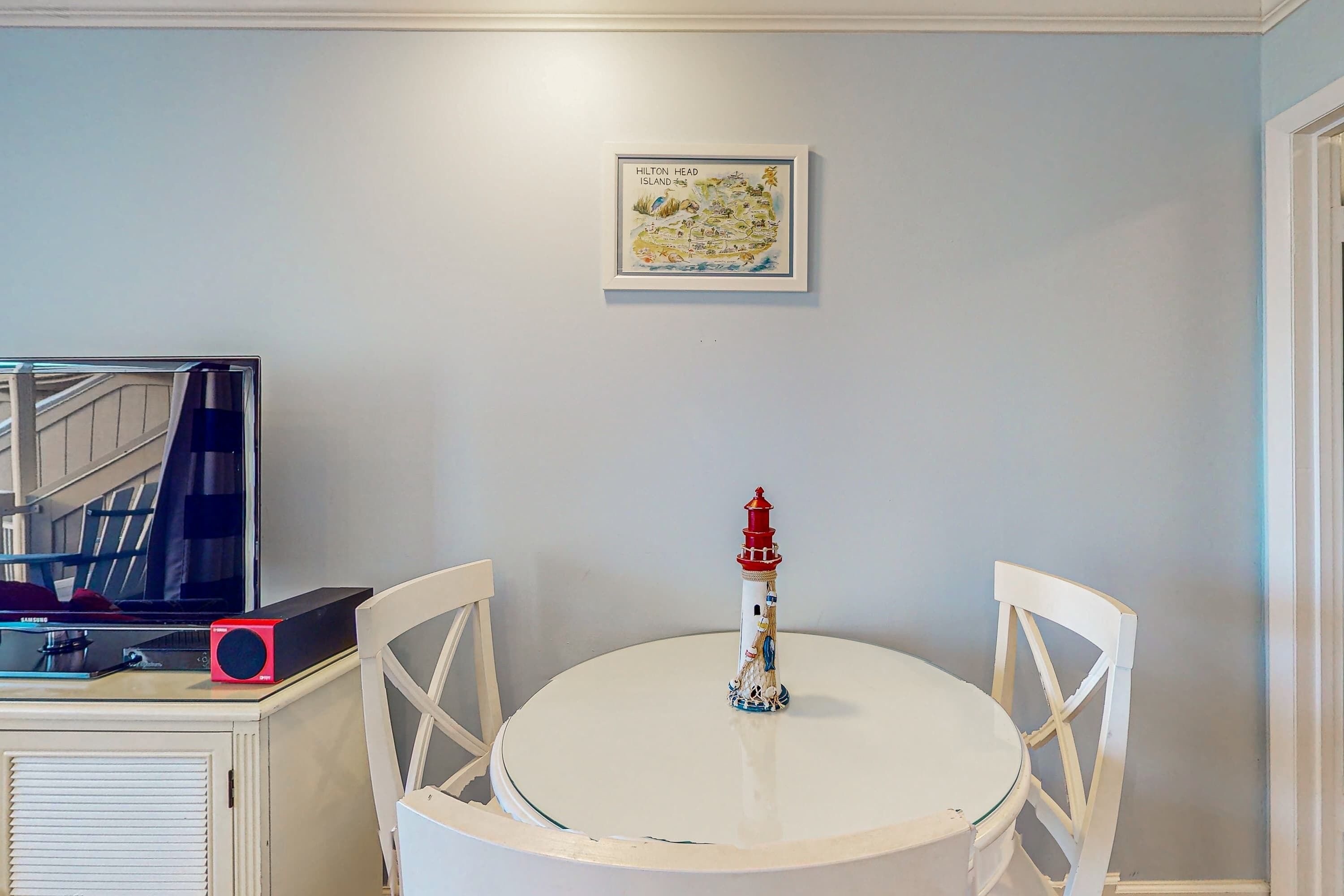 A round table with a white tablecloth, a red and white lighthouse sculpture, and a framed map on the wall.