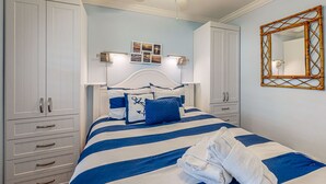 A bedroom with a bed, white wardrobe, bedside lamps, a ceiling fan, and a wall-mounted mirror.
