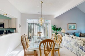 Un comedor con mesa de vidrio y sillas de madera, una sala de estar con un sofá estampado y una lámpara de techo.
