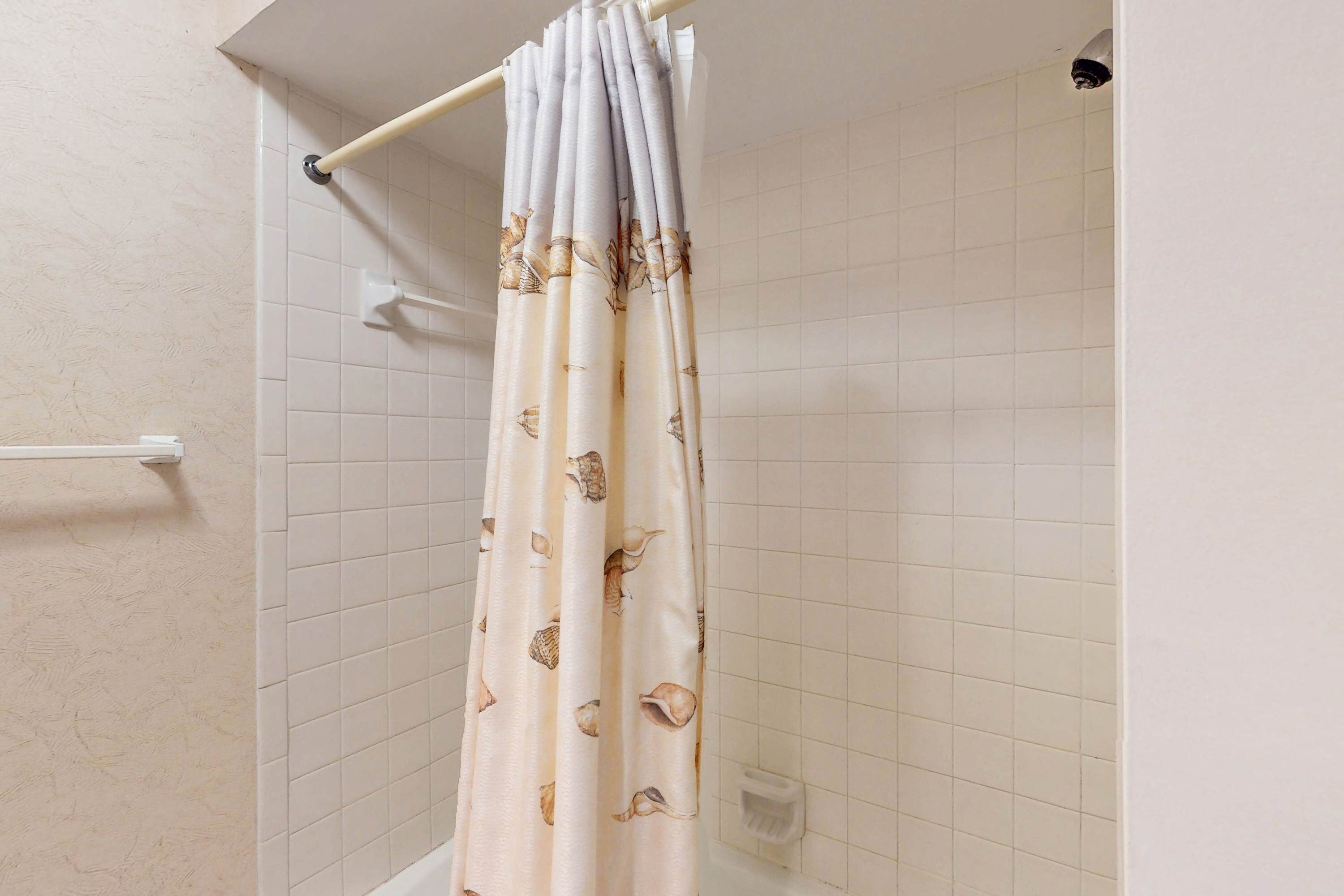A shower curtain with a seashell pattern, a white tiled wall, and a visible shower control panel.