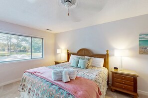 Un dormitorio con una cama, dos mesitas de noche, una lámpara de noche, una ventana y un ventilador de techo.