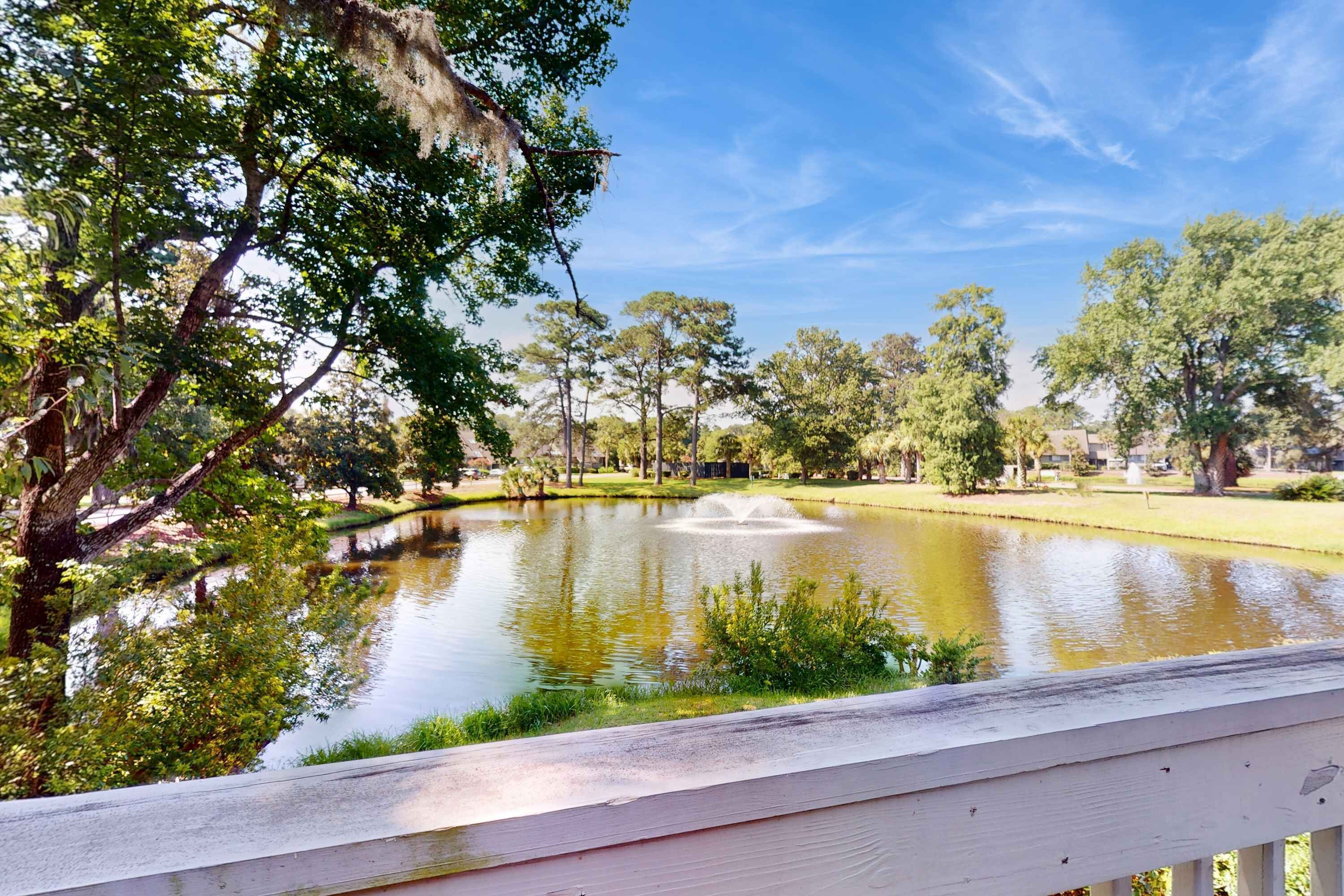 A serene park with a pond, trees, and a wooden deck.