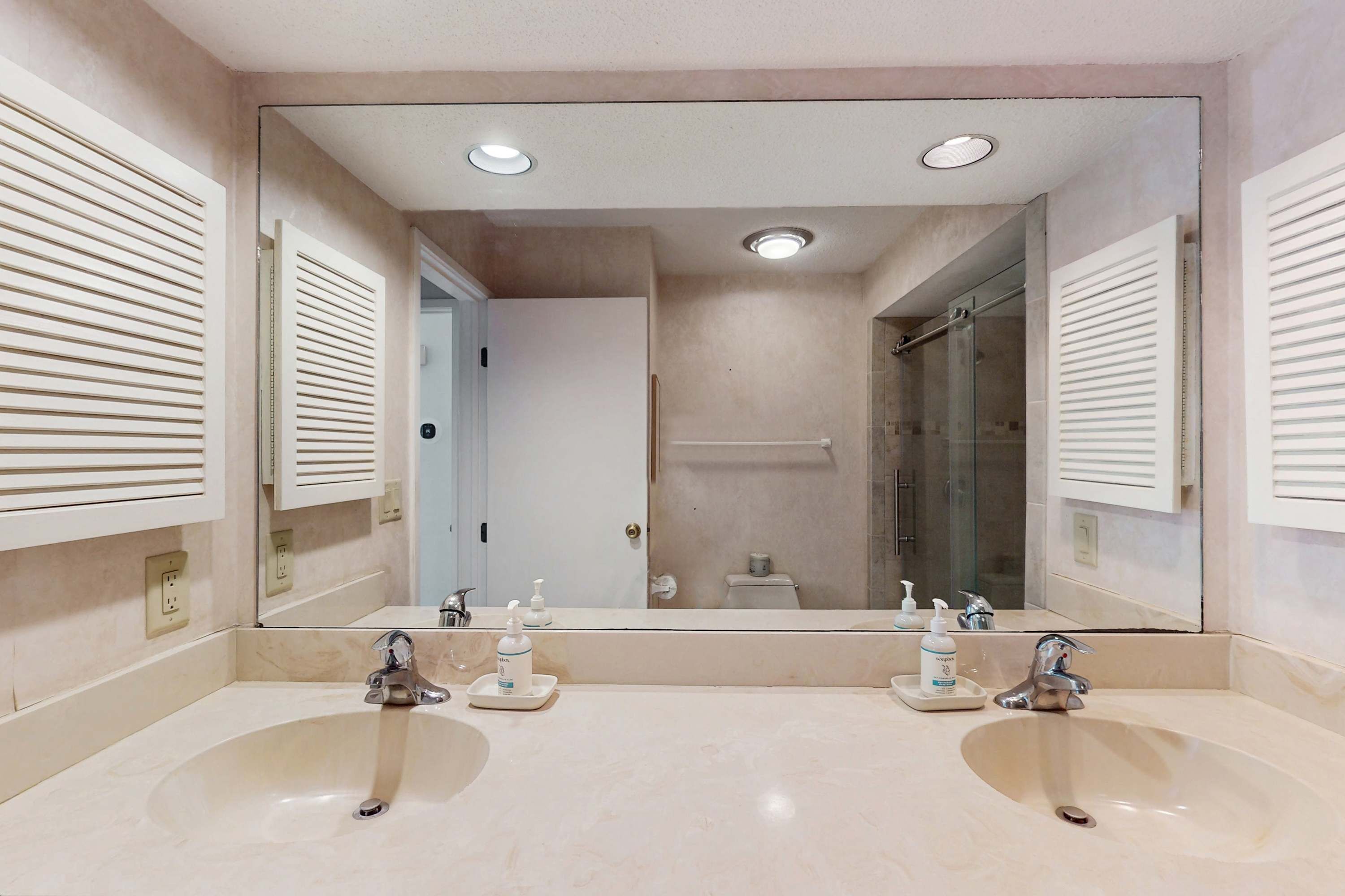 A bathroom with two sinks, a large mirror, and a shower.