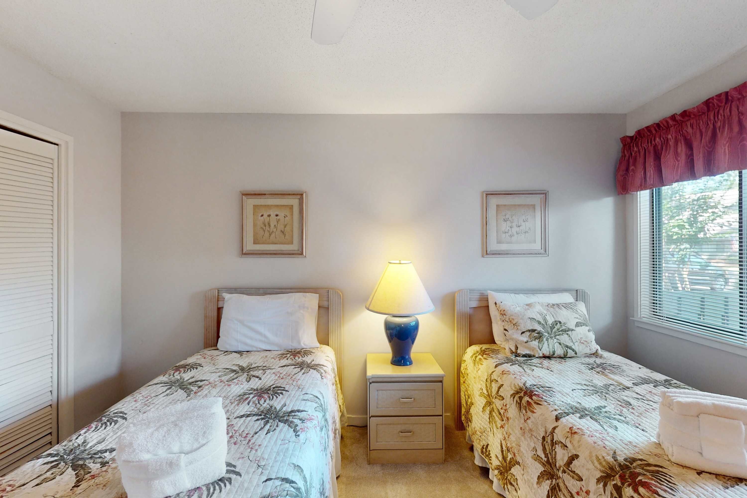 A room with two beds, a nightstand with a lamp, and two framed pictures on the wall.