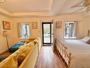 Een kamer met een bed, een bank, een raam en een deur naar buiten.