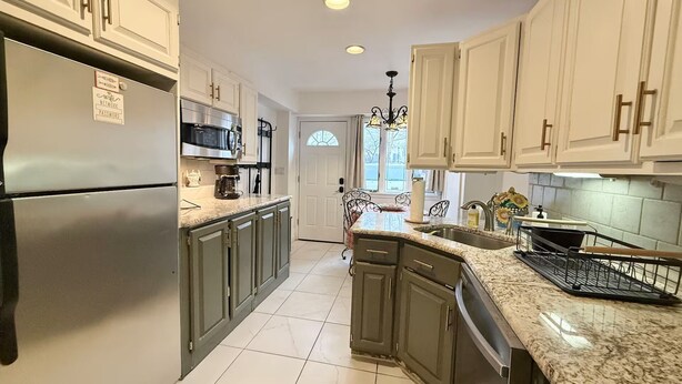 A kitchen with white cabinets, a stainless steel refrigerator, a microwave, and a chandelier. - Cozy Manhattan View Suite (West New York)