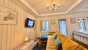 A living room with a sofa, a television, a chandelier, and a window with curtains. - Cozy Manhattan View Suite (West New York)