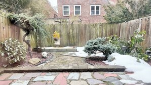 A stone patio with a wooden fence, a small tree, and a statue. - Cozy Manhattan View Suite (West New York)
