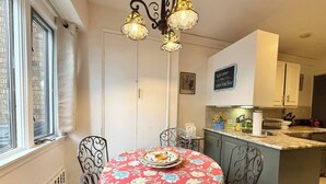 A dining area with a round table, chairs, a chandelier, a kitchen island, and a window. - Cozy Manhattan View Suite (West New York)