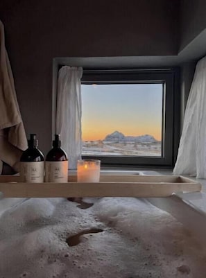A room with a window, a bed, a bedside table with bottles and a candle.