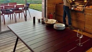 A modern kitchen with a large window overlooking a scenic landscape, a dining area with outdoor seating, and a person cooking at the stove. - Privat lodge, high-end (Nordland)