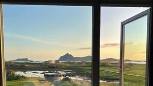 A bedroom with a large window, a bed, and a view of a landscape with mountains and a body of water. - Privat lodge, high-end (Nordland)