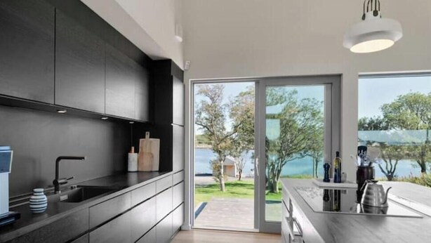 A modern kitchen with dark cabinetry, a large window, and a view of a lake. - Privat lodge, high-end (Nordland)