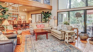 A spacious living area with a high ceiling, a staircase, and large windows offering a view of the outdoors. - 2-story house with private heated outdoor pool, stunning views & foosball (Hilton Head)