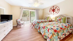 Un dormitorio con cama, televisión, silla, ventilador de techo y ventana.