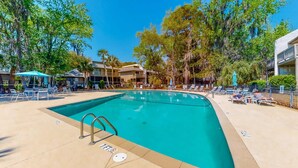 Una piscina con sillones de descanso y sombrillas, rodeada de árboles y edificios.