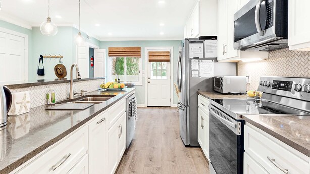 Una cocina moderna con armarios blancos, electrodomésticos de acero inoxidable y un salpicadero con diseño de espiga.