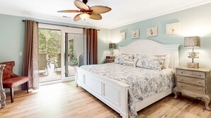 Un dormitorio con cama, una silla, una mesita de noche, una lámpara y un ventilador de techo.