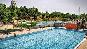A swimming pool with clear water, surrounded by a deck area with people and a hillside in the background. - Monclar Escape With Tennis & Shared Pool (Monclar-de-Quercy)