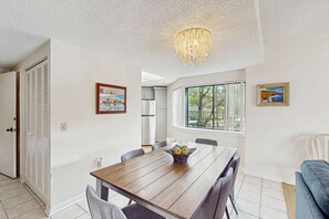 A dining area with a wooden table, chairs, a chandelier, and two framed pictures on the walls. - Inviting family-friendly condo with balcony, central AC, & outdoor pool (Hilton Head)