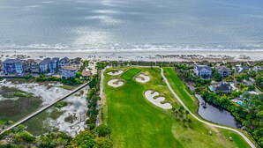 Ett flygbildsbild av ett bostadsområde vid kusten med en golfbana, fastigheter som ligger direkt vid stranden och en bro.