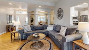 A modern living room with a sectional sofa, a coffee table, and a dining area with a chandelier. - Bright & Expansive Beach Retreat with Private Pool (Hilton Head)
