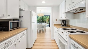 Une cuisine moderne avec des meubles blancs, un four à micro-ondes, une cuisinière et un coin repas comprenant une table et des chaises.