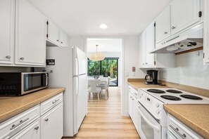 A modern kitchen with white cabinets, a microwave, stove, and a dining area with a table and chairs. - Family Friendly Villa near the Beach, Patio, & Shared Pool (Hilton Head)