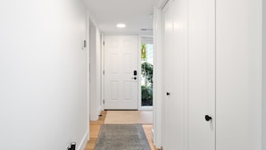 Un couloir étroit aux murs blancs, doté d’un plancher en bois et d’un tapis gris, qui mène à une porte blanche.