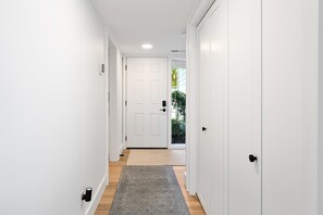 A narrow hallway with white walls, a wooden floor, and a gray rug leading to a white door. - Family Friendly Villa near the Beach, Patio, & Shared Pool (Hilton Head)