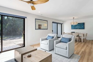 A modern living room with a large sliding glass door, two armchairs, a wooden coffee table, a dining area with a table and chairs, and a ceiling fan. - Family Friendly Villa near the Beach, Patio, & Shared Pool (Hilton Head)