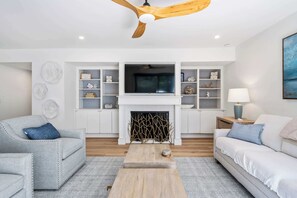 A living room with a fireplace, a ceiling fan, and a TV mounted above it. - Family Friendly Villa near the Beach, Patio, & Shared Pool (Hilton Head)