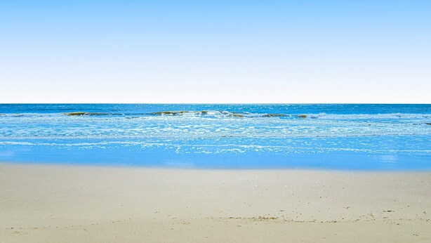 Uma praia com águas azul-claras e areal arenoso.