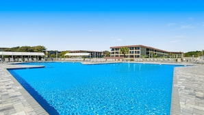 Uma piscina grande com espreguiçadeiras e um edifício ao fundo.