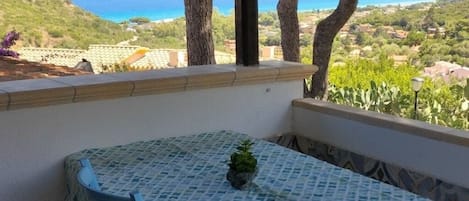 A balcony with a table and chairs, overlooking a coastal landscape with trees and houses.