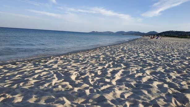 A sandy beach with gentle waves, distant mountains, and a clear sky. - Panoramic Costa Rei (MURAVERA CA)